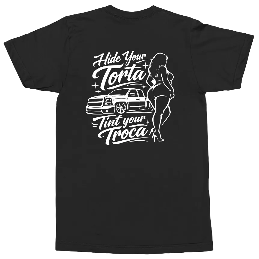 A black short-sleeve t-shirt with a white graphic print on the back. The graphic features the text 'Hide Your Torta Tint Your Troca' in a stylized cursive font, accompanied by a white line-art illustration of a pickup truck and a woman in a bikini.