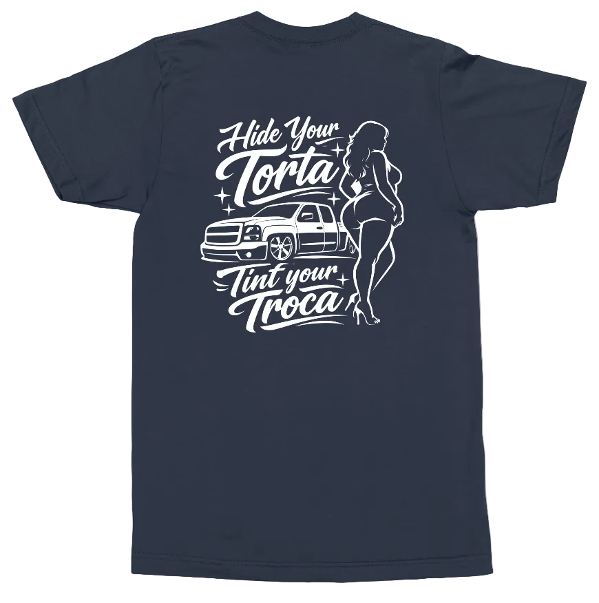 A navy blue short-sleeve t-shirt shown from the back, featuring a white graphic print of a classic pickup truck, stylized text reading 'Hide Your Torta Tint Your Troca', and a woman in a bikini.