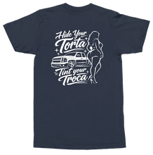 Load image into Gallery viewer, A navy blue short-sleeve t-shirt shown from the back, featuring a white graphic print of a classic pickup truck, stylized text reading 'Hide Your Torta Tint Your Troca', and a woman in a bikini.

