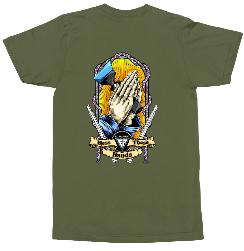 An olive green short-sleeve t-shirt shown flat against a white background, featuring a large graphic print on the back with praying hands, a blue megaphone, swords, and a banner reading 'Hear Us Twice Hands'.