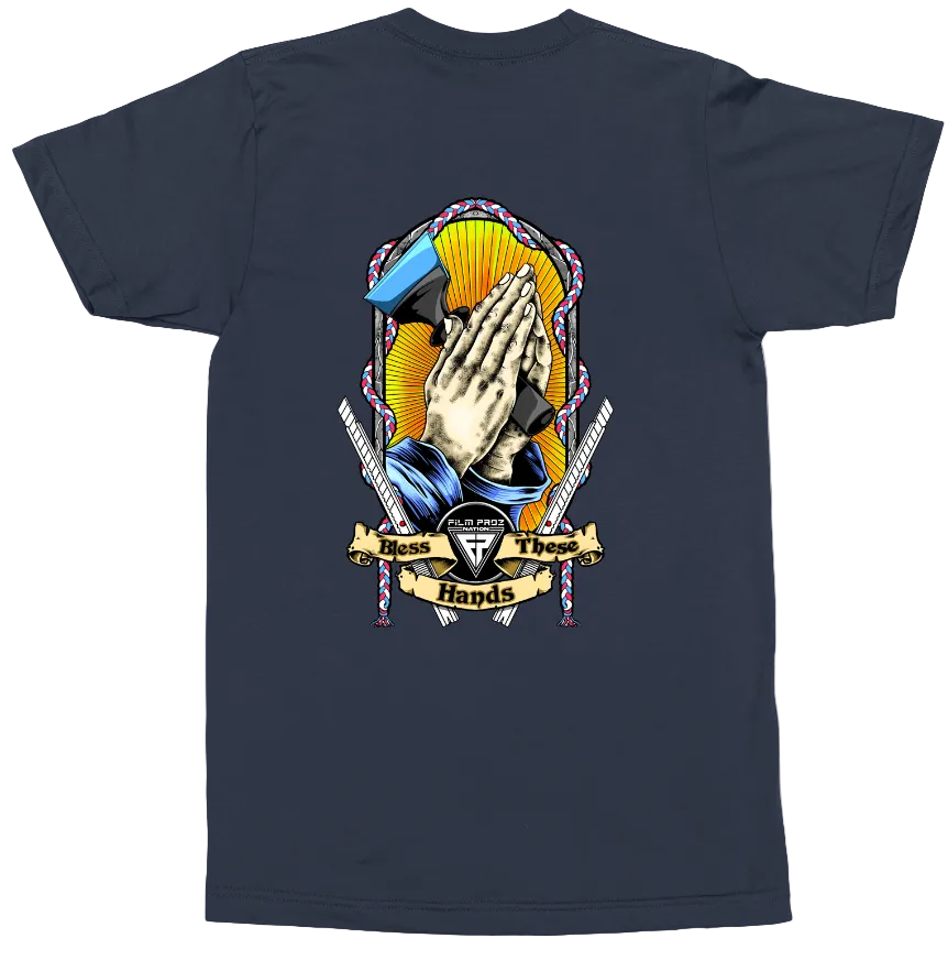 A navy blue short-sleeve t-shirt shown from the back, featuring a large graphic print of a praying hand with a mallet and crossed tools, with a banner reading 'Mass Those Hands' and a central shield logo.