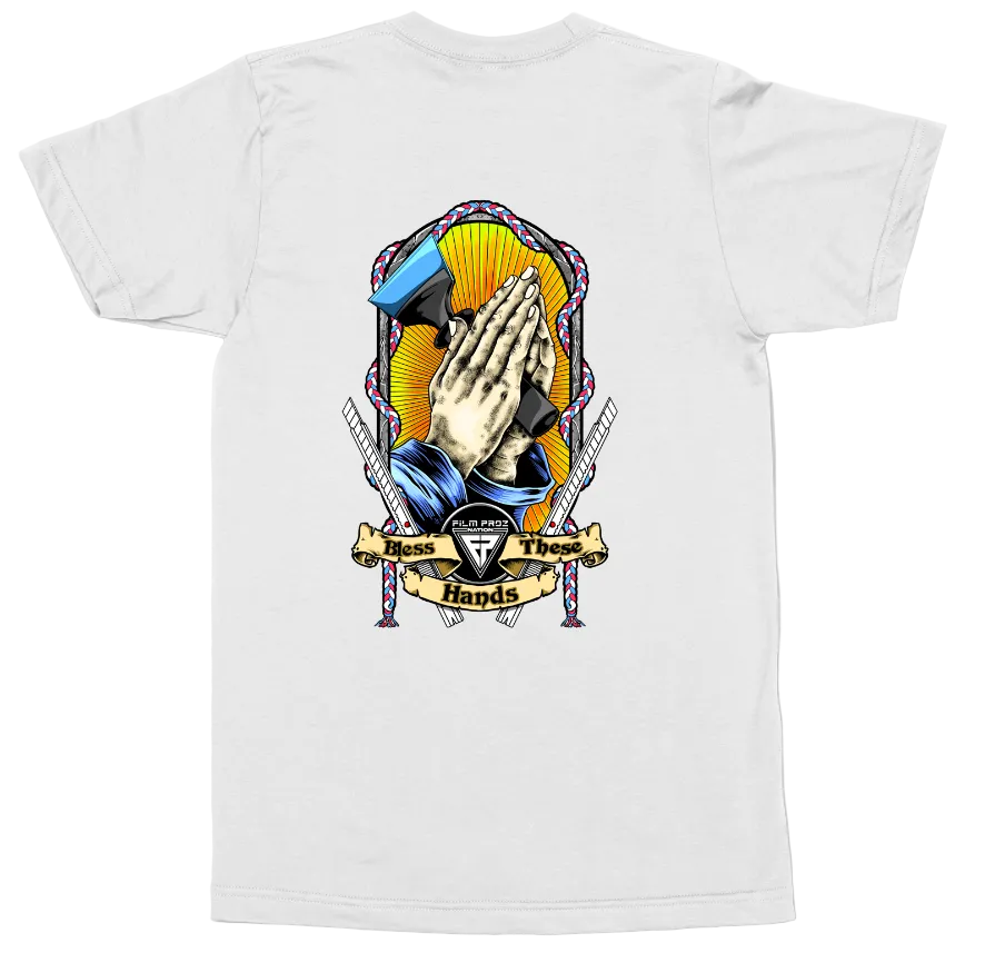 A white short-sleeve t-shirt shown flat against a white background, featuring a large graphic print on the back. The graphic depicts praying hands in the center, flanked by swords and a blue hammer, with a banner reading 'These Too Hands' and a central shield logo.