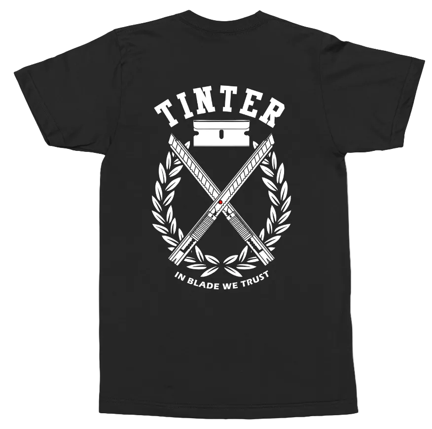 A black short-sleeve t-shirt shown flat against a white background, featuring a large white graphic print on the back with the word 'TINTER', crossed blades, a barbell, and the phrase 'IN BLADE WE TRUST'.