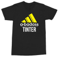 A black short-sleeve t-shirt with a graphic print featuring a yellow Adidas-style logo, the text 'a-badass' in white, and 'TINTER' in white below it, shown on a plain white background.