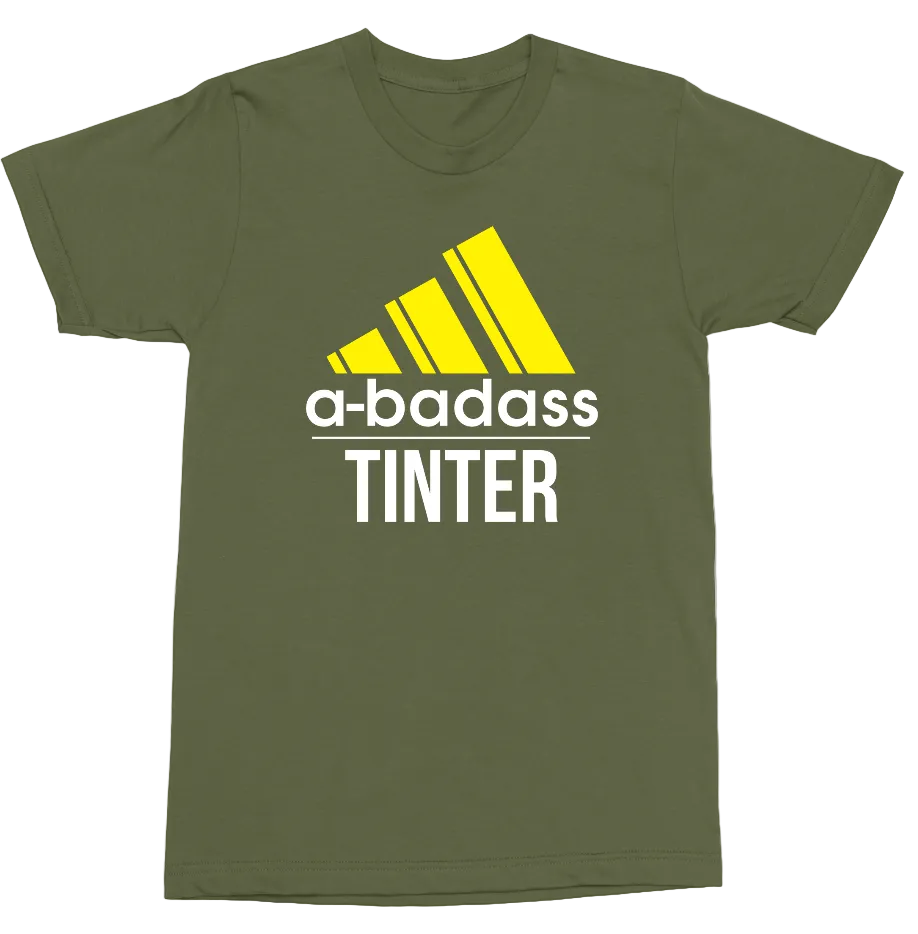 An olive green short-sleeve t-shirt with a graphic print on the front. The graphic features a yellow Adidas-style logo above the text 'a-badass TINTER' in white and yellow.