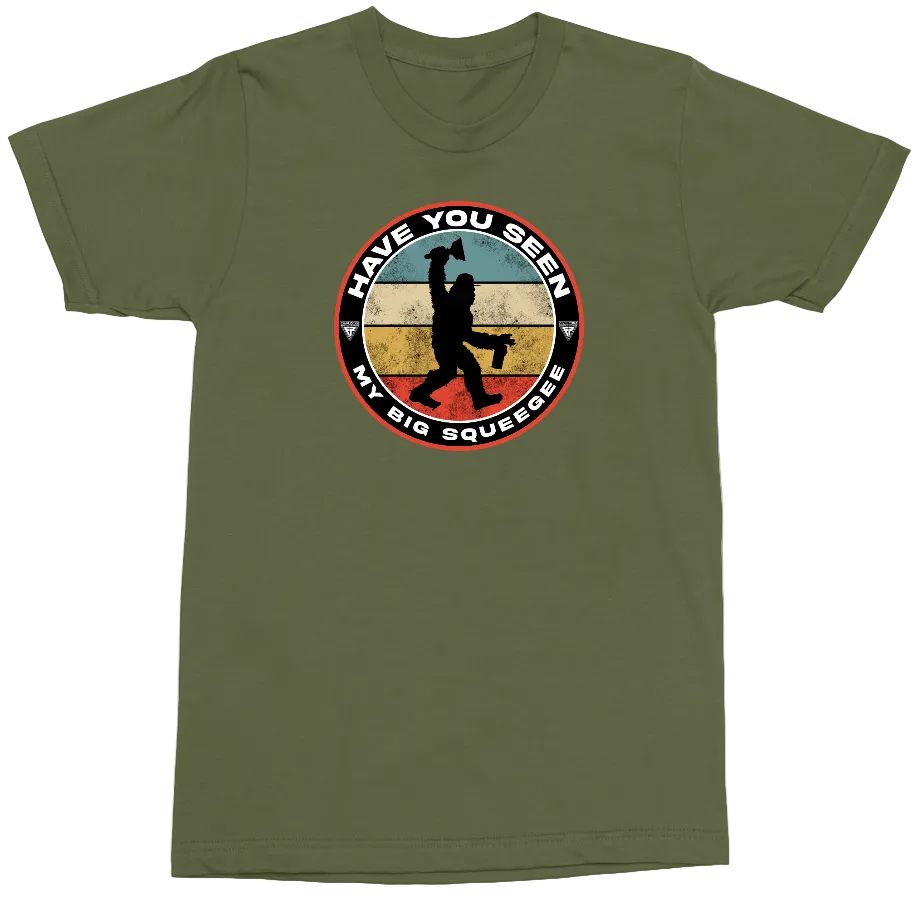 An olive green short-sleeve crewneck t-shirt featuring a circular graphic on the chest with a Bigfoot silhouette and the text 'HAVE YOU SEEN MY BIG SQUEEZEES'.