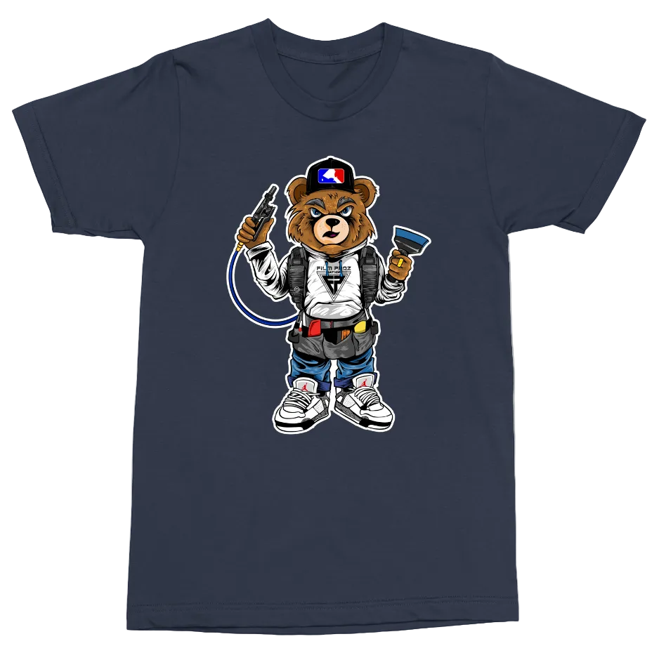 A navy blue short-sleeve crewneck t-shirt featuring a cartoon graphic of a bear character wearing a white hoodie, blue jeans, and sneakers, holding a spray gun and a paintbrush.